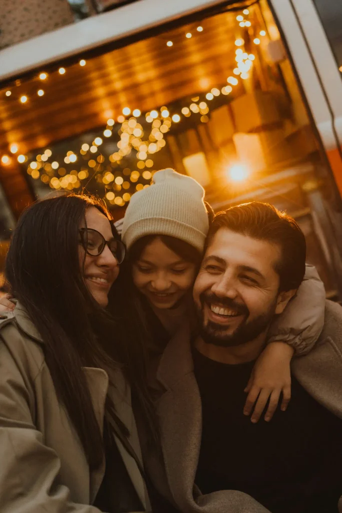 A group of smiling friends huddled together at a party, with string lights in the background