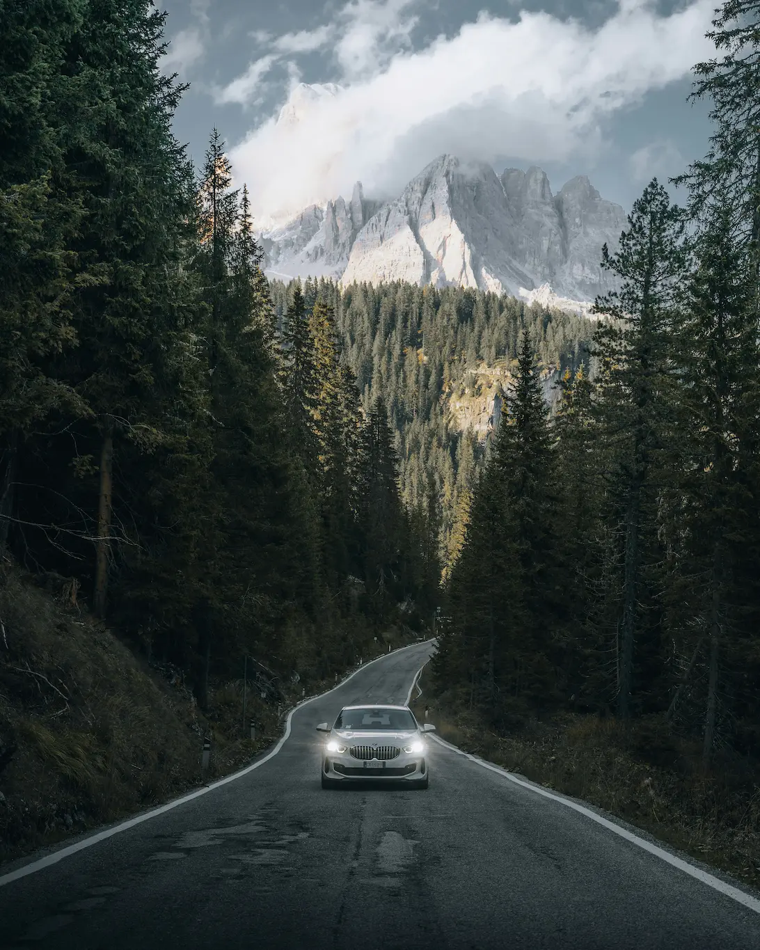 A car driving on a forest road with a snow-capped mountain in the background