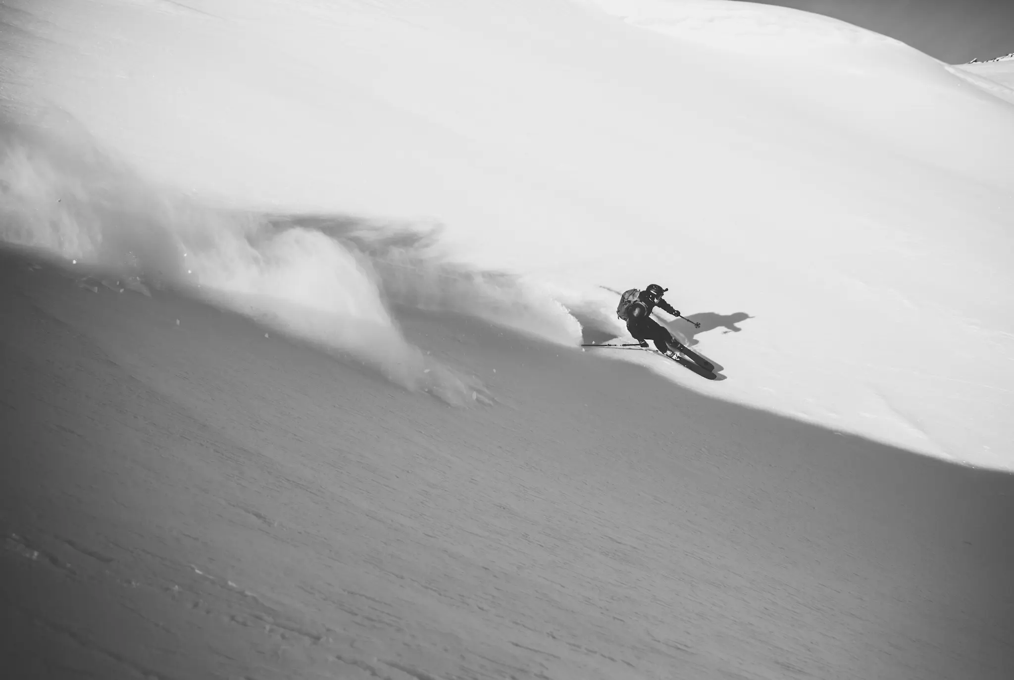 Skieur dévalant une pente enneigée dans un nuage de poudreuse, photo en noir et blanc