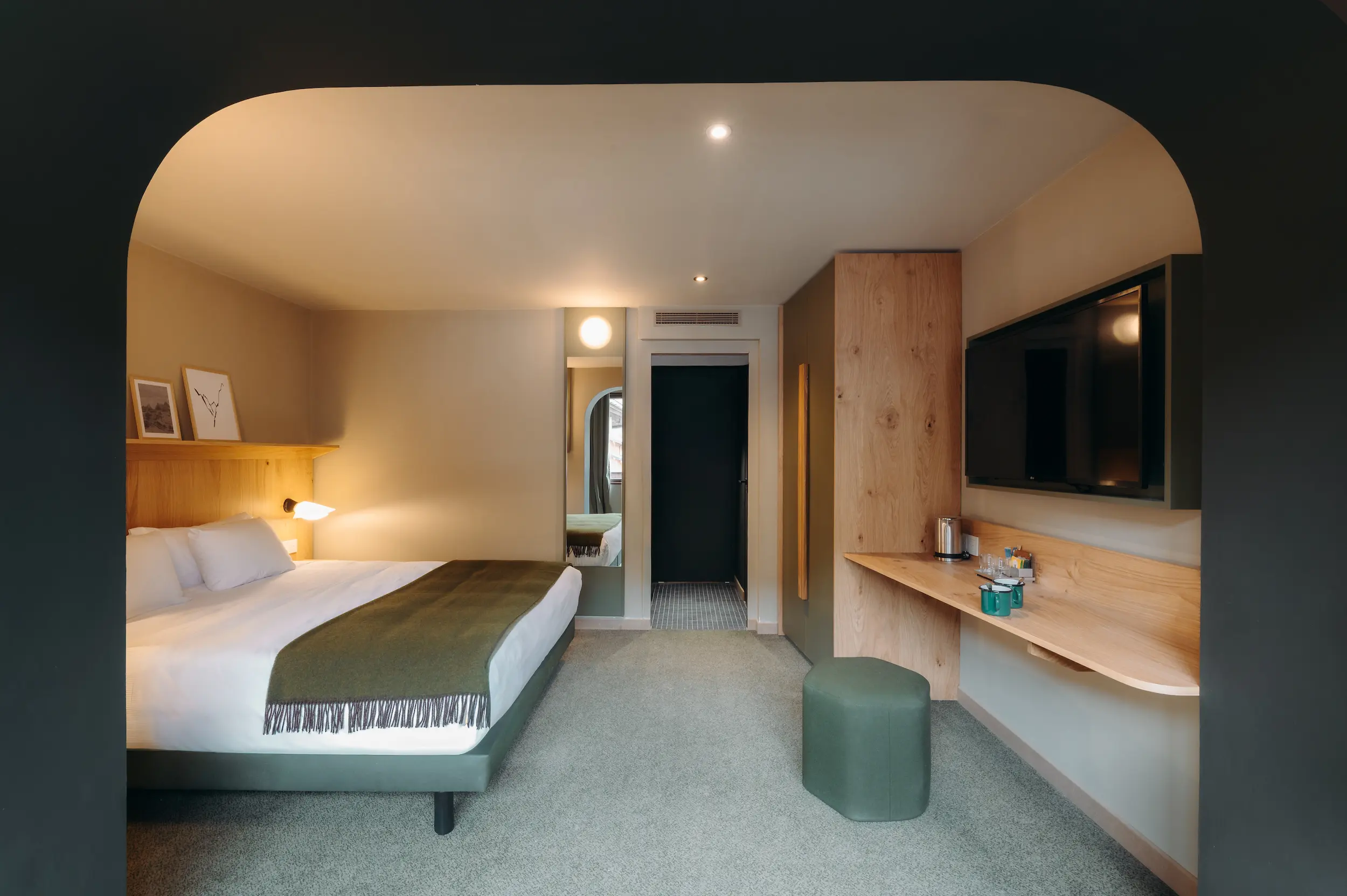 Chambre avec lit, miroir mural, meuble TV en bois et pouf vert, Suite Garance