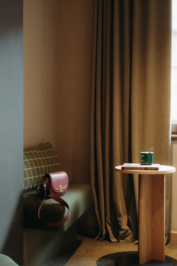 Sac à main en cuir posé sur une banquette, table ronde en bois près d'un rideau, Chambre Familiale