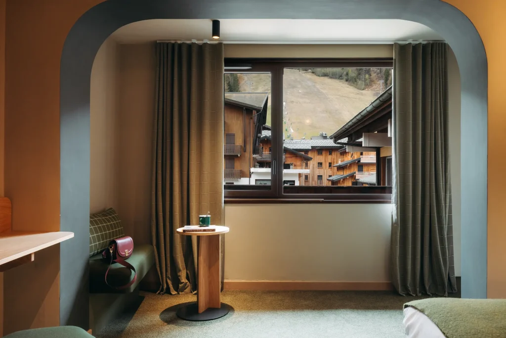 Coin salon voûté avec banquette, table d'appoint ronde et vue sur les chalets et la piste de ski, Chambre Élégance