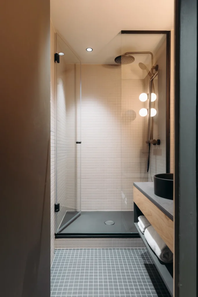 Salle de bain avec douche vitrée, vasque noire et rangement à serviettes en bois