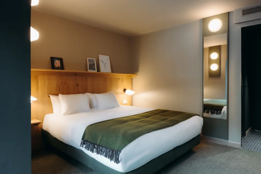 Chambre avec lit, plaid vert à franges et miroir pleine hauteur près de l'entrée, Suite Montagne