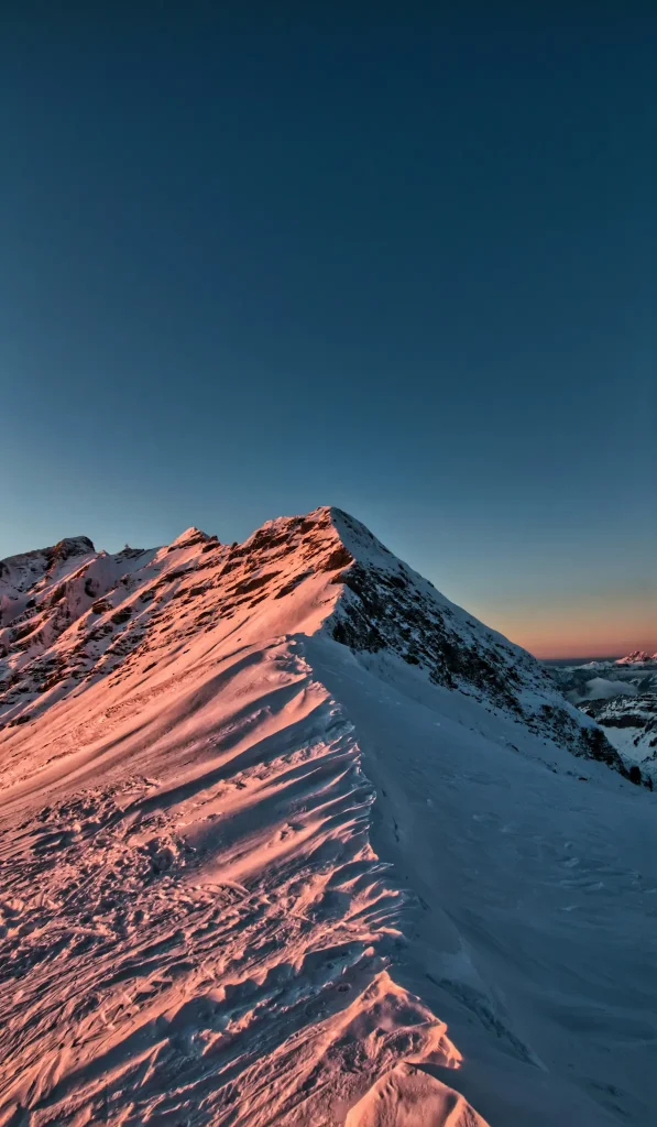 A snow-covered mountain ridge illuminated by the pink light of the sunset
